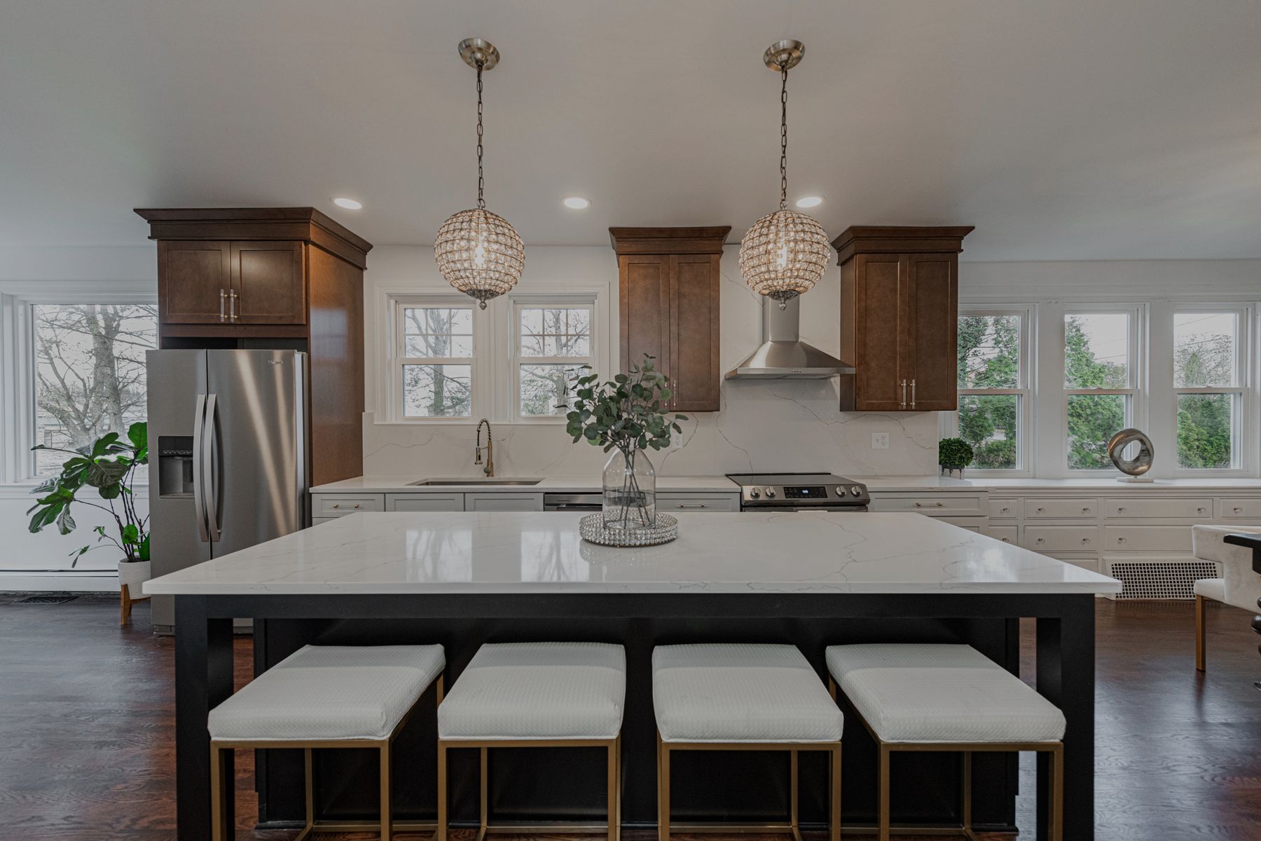 A white kitchen with a quartz island, four stools, walnut cabinets and twin globe pendants